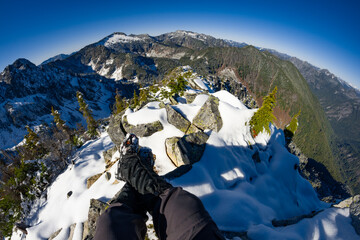 Adventurous athletic male hiker, sitting in a snowy boulder field with his legs outstretched before jagged snowy mountains on a beautiful sunny day.