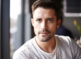 Fototapeta premium Handsome man, portrait and serious face at cafe for morning, ambition or aspiration at indoor restaurant. Attractive or young male person with beard in relax, casual clothing or style at coffee shop