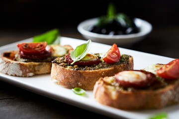 Crostini with tomato, salami and olive pesto on wooden background.