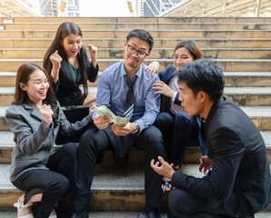 Happiness business people receiving money dollar banknotes after job done and success business deals. A man with eyeglasses holding dollar banknotes and sitting together with excited business team  - 761121728