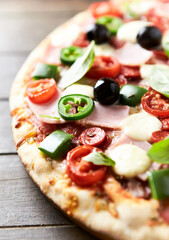 Pizza with ham, mozzarella cheese, cherry tomatoes, green and jalapeno pepper, black olives and fresh basil. Dark background. Close up.	