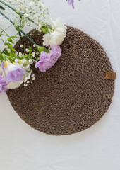 Brown Wicker table napkin and carnation flowers close up. Handmade round tablecloth texture. Organic tableware. Rustic floral decor for home