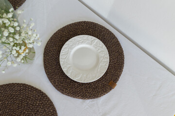 Minimalistic elegant table setting with small glass vase with gypsophila on white plate and knitted...