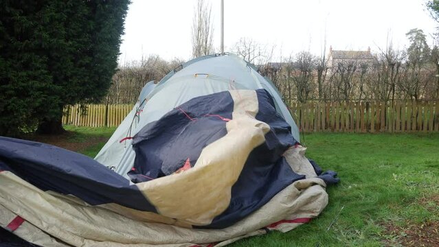 A mature man taking down a tent at a campsite removing the fly sheet on the grass