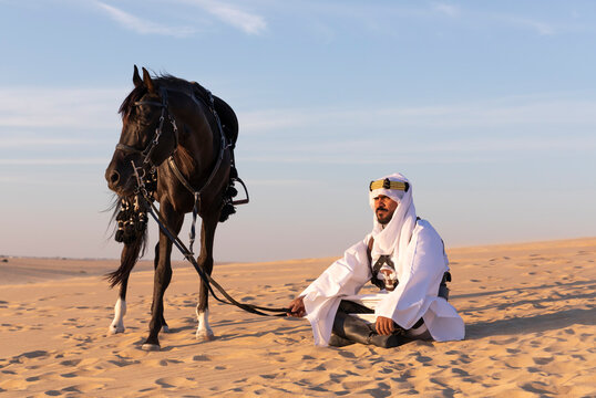 Saudi man in a desert with his black stallion