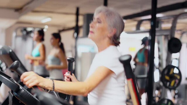 Slender athletic mature woman during cardio exercises on elliptical simulator in fitness center. Sports to max. Electronic tracking for most productive workout