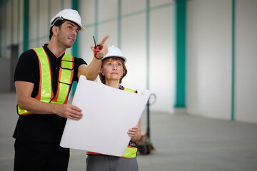 workers or engineers planning from work on blueprint drawing paper and pointing to something in the factory