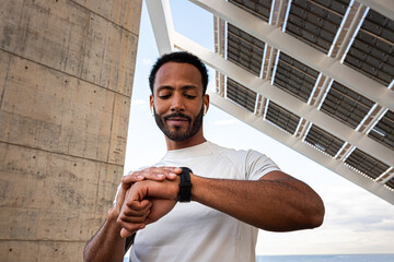 African American man checking pulse in smart watch. Black male with earphones using smart watch to...