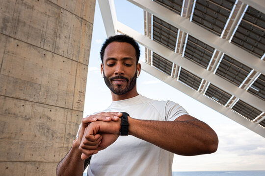 African American man checking pulse in smart watch. Black male with earphones using smart watch to put on music.