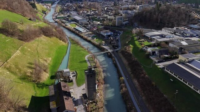 Rolling mill, Linth River and beautiful swiss city between alps at spring season.Building ind blocks with working cranes in backdrop. Aerial tilt up wide shot.