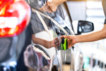 Car polish wax worker hands applying protective tape before polishing. Buffing and polishing car