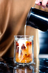 close-up of barista pouring milk into a glass of coffee with espresso, you can see the melting of the liquids