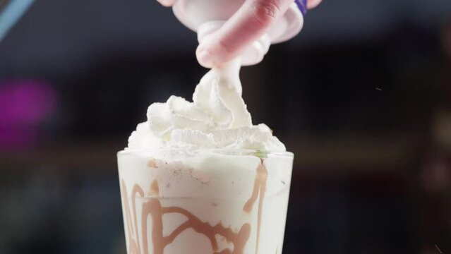 Spraying whipped cream over a chocolate milkshake
