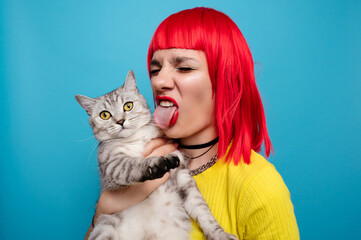 A young beautiful girl with a cat in her arms, isolated on a blue background. Expressive and funny expression on the face. The friendship of the pet and the owner