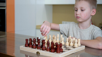 A little fair-haired boy learns to play chess at home. Early development concept. Development of intelligence and brain during leisure games.