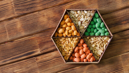 Six varieties of multi-coloured roasted glazed peanuts in a hexagonal kraft box on a rustic wooden...