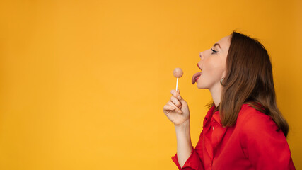 A surprised young funny girl is holding a lollipop in her hands and fooling around. A place for your text.