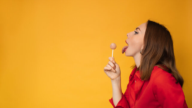 A surprised young funny girl is holding a lollipop in her hands and fooling around. A place for your text.