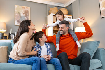 Happy family sitting on sofa laughing together. Cheerful parents playing with their kids at home....