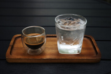 Hot coffee and glass of ice on wooden tray on wooden table