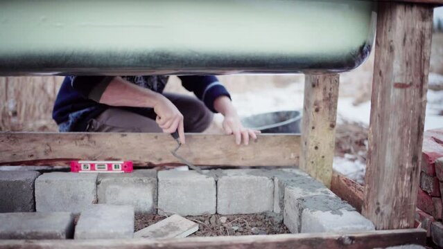 The Man is Using Cement to Fill in the Gaps Between the Concrete Blocks Beneath the DIY Hot Tub - Close Up