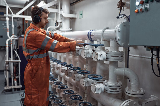 Young marine engineer manually operating valve on valve manifold in engine room.