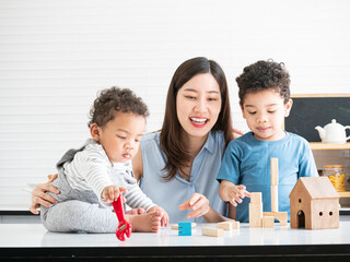Happy young Asian mother playing wooden blocks with two adorable little sons in the living room.Funny educational for children concept.