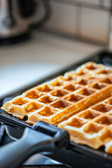 Freshly Baked Belgian Waffles close-up. Golden Belgian waffles sizzle in electric waffle maker iron, delicious breakfast.