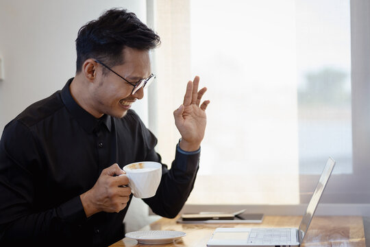 Smiling Asia businessman working on laptop in modern office lobby space. Young indian student using computer remote studying, watching online webinar, zoom virtual training on video call meeting.