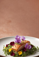 Grilled fish fillet with edible flowers on a white plate.