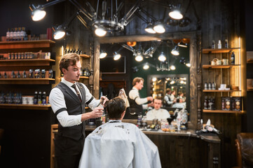 Cropped photo of handsome hairdresser in fancy outfit cutting wet hair. Young customer getting...