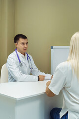 Fototapeta premium Doctor consulting Patient. Professional physician wearing white coat talking to woman at appointment visit in clinic.