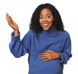 Pregnant African American woman in studio receiving a pleasant surprise, excited and raising hands.