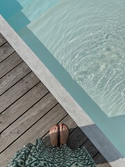 Female feet at poolside. Swimming pool with clear blue water with sunlight shadow reflections on...