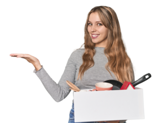 Blonde Caucasian woman moving with a box on studio backdrop showing a copy space on a palm and holding another hand on waist.