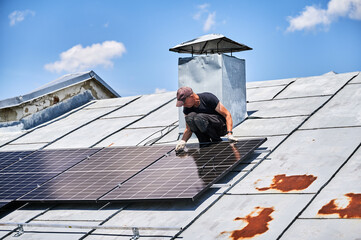 Worker building photovoltaic solar panel system on metal rooftop of house. Man engineer installing...
