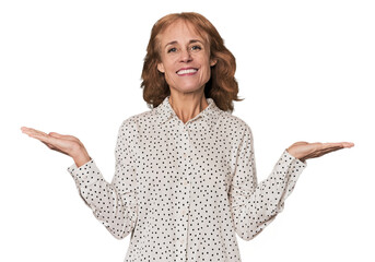 Redhead mid-aged Caucasian woman in studio makes scale with arms, feels happy and confident.