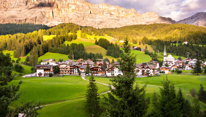 Mountain village with a church in Dolomite alps in summer among green meadows