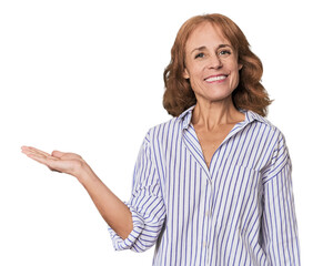 Redhead mid-aged Caucasian woman in studio showing a copy space on a palm and holding another hand...