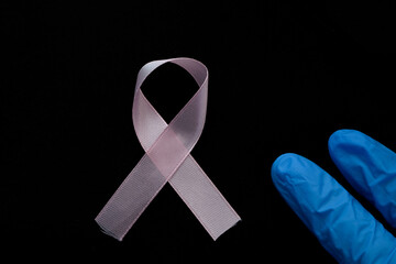 Dłoń w niebieskiej rękawicy medycznej pokazuje różową wstążkę, walka z rakiem piersi - obrazy, fototapety, plakaty