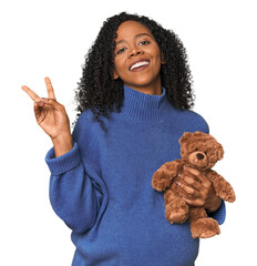Expecting African American with teddy bear joyful and carefree showing a peace symbol with fingers.
