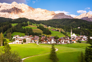 Naklejka premium Mountain village with a church in Dolomite alps in summer among green meadows