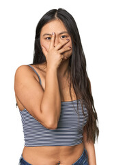 Young Chinese woman in gray top, studio blink at the camera through fingers, embarrassed covering face.