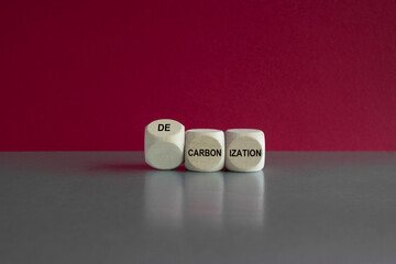 Symbol to reduce carbon dioxide. Turned wooden cubes and changes words carbonization to decarbonization. Grey table, red background, copy space. Business concept.