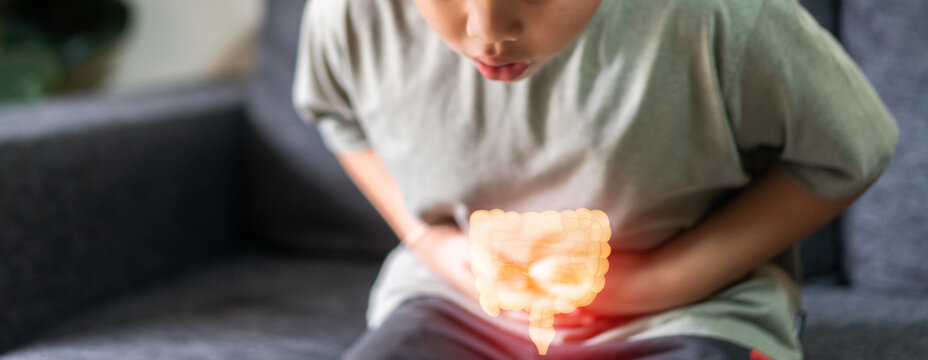 Portrait of sick unhappy little child asian boy touching belly stomach with suffering from stomach ache pain, gastritis, gastroenteritis, food poisoning, diarrhea, intestinal inflammation at home