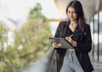 Confident businesswoman using digital tablet while standing outside office. Long hair beautiful business woman working outdoor checking information online. Success female CEO entrepreneur in suit.