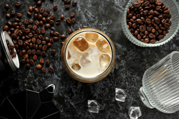 Glass with iced coffee drink, coffee maker and coffee bean on gray background, top view