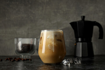 Glass with iced coffee drink, coffee maker and coffee bean on gray background