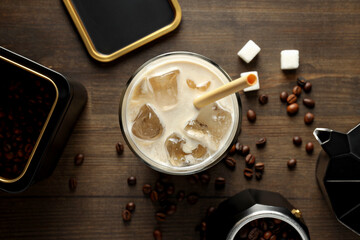 Glass with iced coffee drink, coffee maker, coffee bean and sugar on wooden background, top view