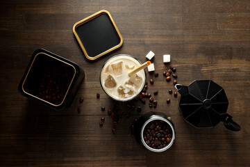 Glass with iced coffee drink, coffee maker, coffee bean and sugar on wooden background, top view